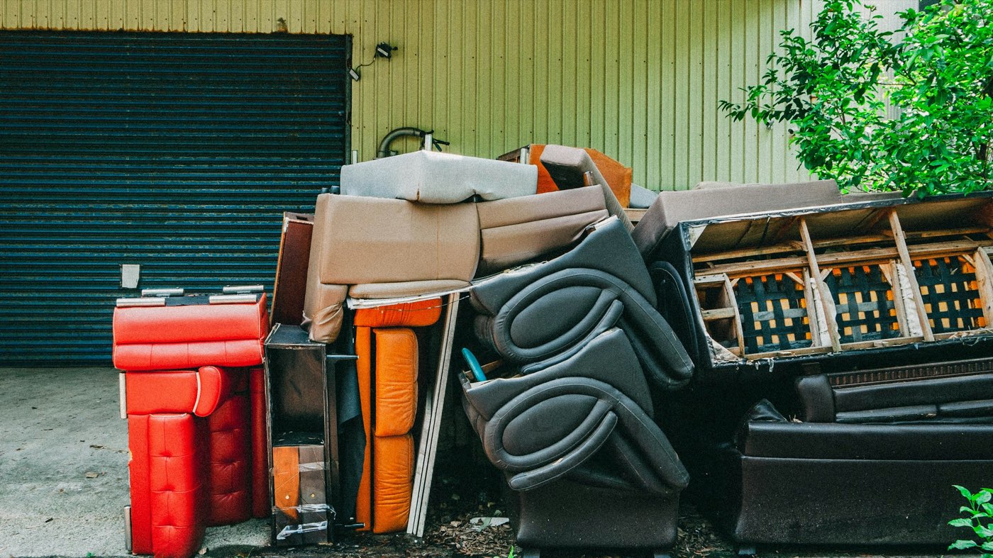 A pile of discarded couches, chairs and mattresses stacked outside a building, waiting for pickup